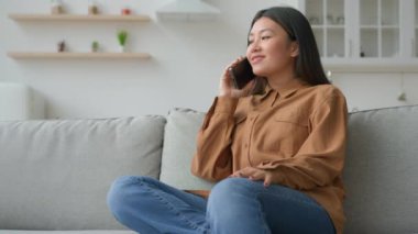 Asyalı kadın mutfakta cep telefonuyla konuşuyor çevrimiçi teslimat servisini arıyor akıllı telefonla konuşup sipariş veriyor Japon Çinli kız gülümsemesiyle iletişim kuruyor.