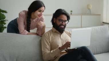Dizüstü bilgisayarı olan Hintli Müslüman koca, arkasında kadın karısıyla konuşuyor. Mutlu Arap farklı etnik çiftler İnternet siparişi alışverişlerini tartışıyor İnternet üzerinden alışveriş uygulamasında emlak dairesini seçiyorlar