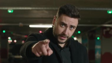 Beyaz adam, el kol hareketi yapan erkek işadamı, yer altı otoparkındaki şoför seni seçen kameraya davetkar parmakla parmak işareti yaparak buraya davet ediyor.