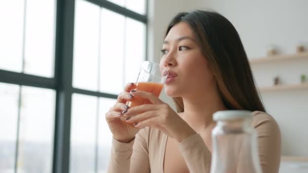 キッチンで中国人アジア人女性飲むガラス新鮮なオレンジ桃ジュース笑顔の女の子離れて夢を見て自然果物野菜スムージーを楽しむ健康的なリフレッシュメントの減量のデトックスリラックス — ストック動画