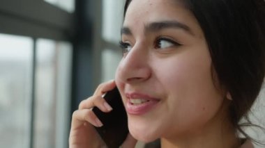 Kafasını kapat, Arap kızı konuşuyor pencerenin yanında cep telefonu konuşuyor gülümseyen kadın iş kadını konuşuyor ev ofisinden Hintli kadını arıyor gülüyor, akıllı telefonlardan uzak konuşmalar yapıyor.