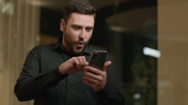 Ofiste cep telefonu kullanan erkek işadamı şok oldu. Piyango ikramiyesi kazandı. Heyecanlı beyaz adam iş fırsatı kazandı.