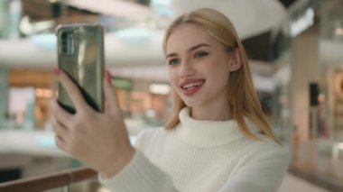 Kafkasyalı kadın blogcu video konuşması çevrimiçi cep telefonu kayıtları alışveriş merkezindeki akıllı telefondan canlı yayınlanıyor. Gülümseyen mutlu kız müşteri müşterisi arkadaşlarıyla konuşuyor.