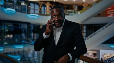 Orta yaşlı Afrikalı Amerikalı girişimci etnik adam kapalı mekanda iyi haberleri cep telefonuyla dinlerken zafer konuşmaları yaparken akıllı telefon kazanmak mutlu iş konuşmaları