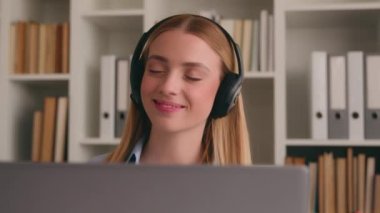 Kafkasyalı mutlu kadın ofis çalışanı kulaklıkla müzik dinleyip dizüstü bilgisayarla dans etmekten zevk alıyor. Neşeli iş kadını. Kulaklıkla müzik dinliyor. Eğleniyor.