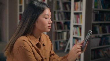 Üniversite kütüphanesindeki Asyalı kız öğrenci internet konferansında çalışan cep telefonu kullanarak akıllı telefon üniversite eğitimi hocasıyla uzaktan iletişim kuruyor.