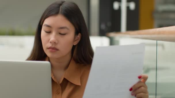カフェビジネスモールで書類を扱うアジアのビジネス女性中国人韓国人女性はローン請求書を読みます文書日本の女の子フリーランス会計士は ノートパソコンのカウント財務上でオンライン請求書のクレジット税を支払う — ストック動画