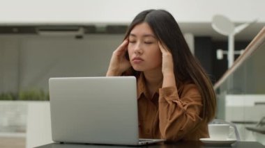 Bitkin düşmüş Asyalı Çinli Japon öğrenci kız öğrenci kafeteryada dizüstü bilgisayarla çalışıyor. Yorgun iş kadını. Düşünmesi zor bir karar.