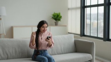 Kanepedeki aşırı neşeli kadın kız. Cep telefonu kullan. Heyecanlı müşteri e-ticaret alışverişi yapıyor. Teklif alıyor.