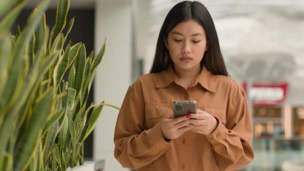 Asiática Mulher Focada Andando Shopping Center Com Smartphone Olhar Para — Vídeo de Stock