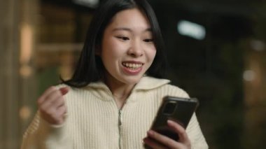 Alışveriş merkezindeki heyecanlı Asyalı kadın müşteri internet indirimi cep telefonu uygulamasını kazandı mutlu Çinli Koreli kız zafer e-ticaret karı hediye ikramiyesini kutladı
