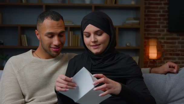 多人種カップルアフリカ系アメリカ人の夫イスラム教徒の妻でHihab励起家族の女性男性オープンメール封筒読み取り紙の手紙銀行通知お祝い良いニュースウィンハウス住宅ローンオファー金融賞 — ストック動画