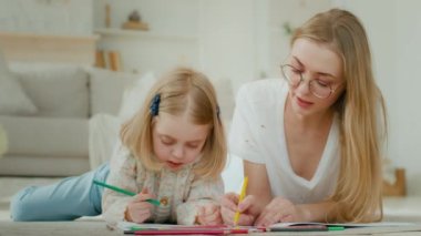 Kafkasyalı anne evde yerde yatarken gözlük takıyor ve evlat edinilmiş küçük bir kız çocuğu birlikte resim çekmekten zevk alıyor. Annesiyle anaokulundaki kız bebek bakıcısı kalemlerle resim çiziyor.