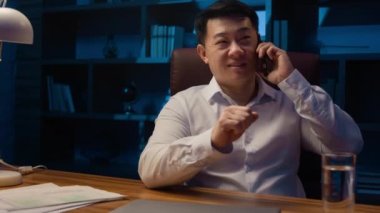Mutlu Asyalı işçi yönetici yönetici yönetici yönetici girişimci gece ofisinde cep telefonuyla konuşuyor. Koreli iş adamı Çinli şirket CEO 'su Japon yatırımcı akşam geç saatlerde akıllı telefon konuşması yaptı