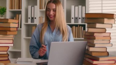 Gülümseyen mutlu Kafkasyalı öğrenci kız üniversite öğrencisi kaygısız kadın dizüstü bilgisayarla ve kitaplarla çalışıyor ödev yazıyor öğrenme tebessümü yazıyor ev kütüphanesinde sınav sınavlarına hazırlanıyor.
