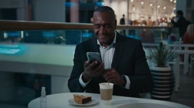 Mature adult middle-aged ethnic African American businessman man sitting in cafe with coffee tea and slice of pie cake make photo selfie with mobile phone camera posing for smartphone image shooting