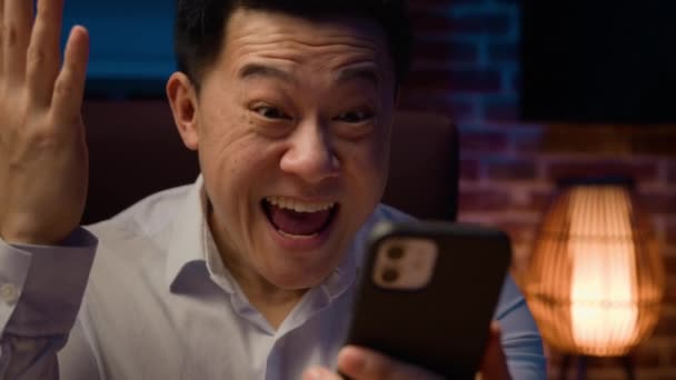 携帯電話の勝利と幸せな笑顔の興奮した勝者アジアの男の勝利は モバイルベットを獲得して叫んで叫ぶ韓国のビジネスマンは 夜のオフィスで良いニュースビジネスの提供スマートフォンの成果を受け取る達成 — ストック動画