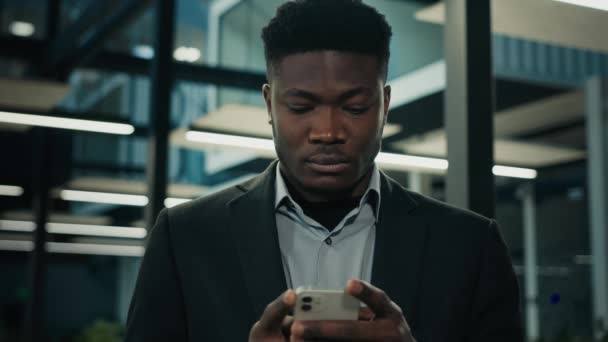 アフリカのビジネスマンは 携帯電話のデジタルアプリを使用して オフィスでスマートフォンを持つ携帯電話悲しい失望男性従業員に民族的なアメリカの男性専門家の執行役員のテキストメッセージを集中 — ストック動画