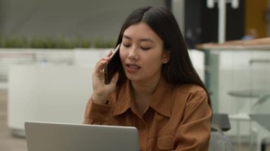 Asyalı iş kadını birden fazla işte çalışıyor. Bilgisayarlı konuşma cep telefonu internet projesini kullan. Kafede gülümseyen Çinli Çinli bir kızla sohbet eden Çinli bir kız.