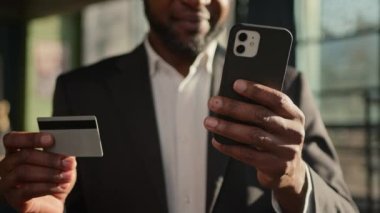 Kredi kartını kapat. Kimliği belirsiz Afrikalı Amerikalı yetişkin işadamı bankacı cep telefonu parasını internet üzerinden ödüyor. Alışveriş ekommersini finanse ediyor.