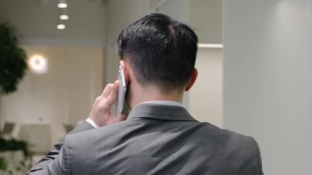 戻る廊下オフィスでビジネスマンの散歩を表示携帯電話を話す 中国人のアジア人の後ろに頭を回します中国人の男エグゼクティブマネージャー中年の上司は スマートフォンの交渉ビジネスコミュニケーションを議論話す — ストック動画