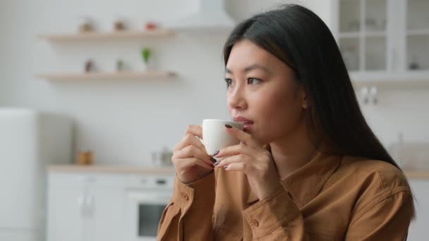 安详悠闲的亚裔中国女人坐在厨房里喝杯茶梦想着和谐的感觉喝着韩国语女孩喝着香气咖啡体贴的家庭主妇在家里放松 — 图库视频影像