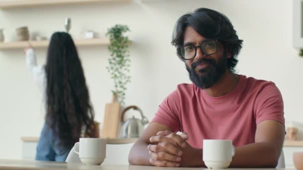 快乐的大胡子男人的丈夫坐在厨房里穆斯林印度男人笑容满面 而女人则在做饭做饭 已婚阿拉伯裔夫妇在家做饭 — 图库视频影像