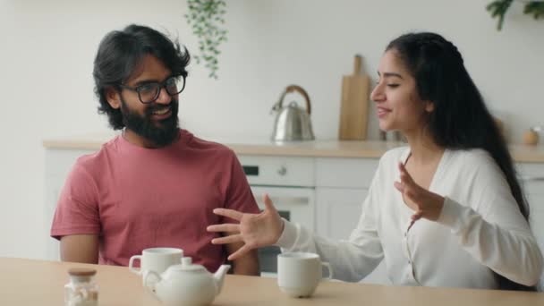 アラビア語インディアンカップルでキッチンでコーヒー共有ニュース多人種の多様な女性の妻と男の夫話し合いの計画一緒に感情的な興奮した女の子教えて面白い話笑いトークで自宅 — ストック動画