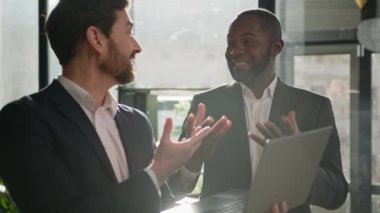 İki çok ırklı erkek iş ortağı çok ırklı iş adamları Afrikalı Amerikalı yönetici ofis çalışanı ve Kafkasyalı işveren lideri keyifli sohbetler dizüstü bilgisayarın keyfini çıkarın iyi iş projesi sonuçları