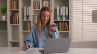 Bilgisayarda dizüstü bilgisayarla çalışan, cep telefonuyla konuşan, hoparlörden konuşan, mutlu iş kadını notlar yazan, sesli mesaj kaydeden çok görevli beyaz bir kadın.