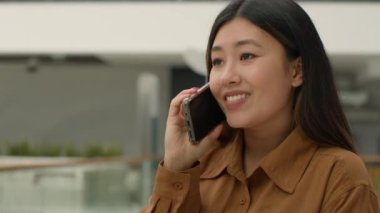 Ofiste cep telefonuyla konuşan mutlu Asyalı kadın cep telefonu Çinli iş kadını cep telefonuyla konuşuyor cep telefonu görüşmesi yapıyor uzaktan iletişim kuruyor neşeli gülümsemeli bayanla konuşuyor gülüyor