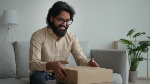 快乐的男性顾客客户消费者阿拉伯印度男人戴眼镜打开纸板箱在家里打开包装网上购物定单购买包裹收件送礼拆箱包裹 — 图库视频影像