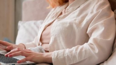 Tembel, serbest çalışan, beyaz bir kadın sabah yatağında laptopla çalışıyor. Ev odasından uzakta çalışıyor. İnternetten alışveriş uygulamasında gülümseyen bir bilgisayarla sohbet ediyor.