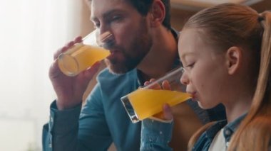 Evde portakal suyu içen mutlu bir aile küçük kızıyla birlikte beyaz bir baba kahvaltıda sağlıklı meyve suyu içiyor çocuk kızıyla konuşuyor organik sulu vitamin içeceklerinin tadını çıkarıyor.