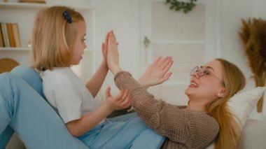 Evde mutlu bir aile var. Kafkasyalı bir anne ve tatlı bir kız çocuğu kanepeye uzanmış kek oynuyorlar. Anne ve küçük kız el çırpıyorlar.