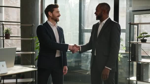 两个不同种族的商人的商业伙伴在办公室里握手 对着镜头微笑的白人和非裔美国人握手 达成协议 — 图库视频影像