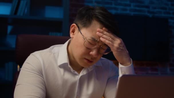 自宅のオフィスで夜のノートパソコンで働く眼鏡でストレスアジアのビジネスマン疲れ韓国の中高年男性過労幹部は頭痛の痛み片頭痛のストレスビジネスの失敗を感じる — ストック動画