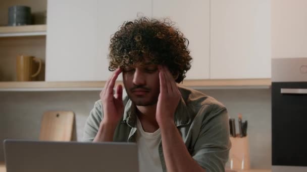 疲れフリーランス男性インド人男性受信悪いニュース通知障害失われたアラビア人男苦しむ片頭痛痛み頭の痛み頭痛コンピュータOverworkビジネス問題とともにラップトップでホームキッチン — ストック動画