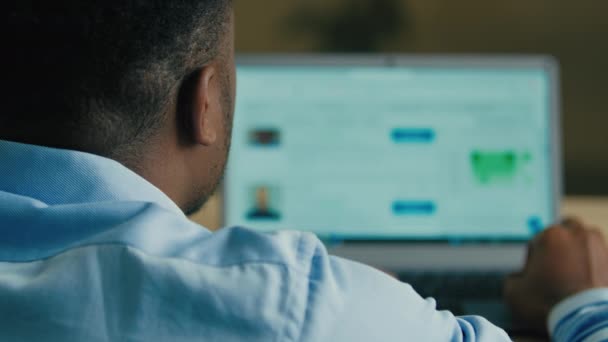 肩に戻るビューの上に認識できないアフリカ系アメリカ人男性ビジネスマンフリーランスの従業員検索ソーシャルメディアビジネスネットワーク見ますノートパソコン画面スクロールウェブサイト上のコンピュータ上のホームオフィス — ストック動画