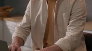 Hareket eden Kafkasyalı yorgun adam mutfakta dizüstü bilgisayar başında fazla çalışıyor bilgisayarlı serbest çalışan erkek göz ağrısı çekiyor gözlük takmak, gözlük takmak görüşü bozuyor.