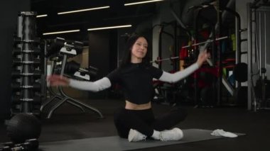 Spor giyim antrenmanında formda olan mutlu bir kadın. Aktif, esnek, beyaz kadın sporcu kız antrenör jimnastik yapıyor. Gergin kasları spor kulübünün spor salonunda spor paspasına oturmuş gülümsüyor.
