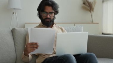 Hintli Müslüman adam evde dizüstü bilgisayarda çalışıyor Arap işadamı, belgeleri analiz ediyor evrakları okuyor, faturaları ödüyor banka hesaplarını internet üzerinden ödüyor kira ödemelerini hesaplıyor.