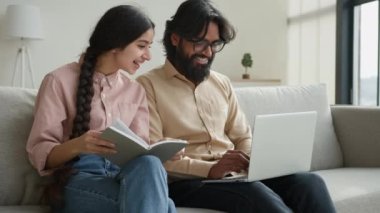 Dizüstü bilgisayarlı çift ev bütçesi planlayan ev kredisi ödemelerini ödemeli Arap kadın karısı not defterinde Hintli adam kocası evdeki bilgisayar aile işleriyle ilgili veri e-postaları yazıyor.