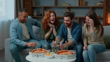 Mutlu çok ırklı arkadaşlar bayram kutlamalarını kutluyor. Bira şişeleri, pizza siparişleri, yemek siparişleri, kanepeye otur. Kadınlar ve erkekler, hafta sonları gülerek dinleniyorlar.