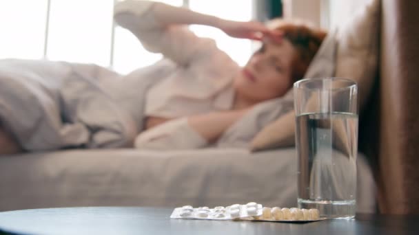 一杯水和治疗在卧室桌上的药物模糊生病的女人头痛在床上女人头疼的头偏头痛偏头痛宿醉痛症烟熏考拉威斯女孩服用止痛药止痛药 — 图库视频影像