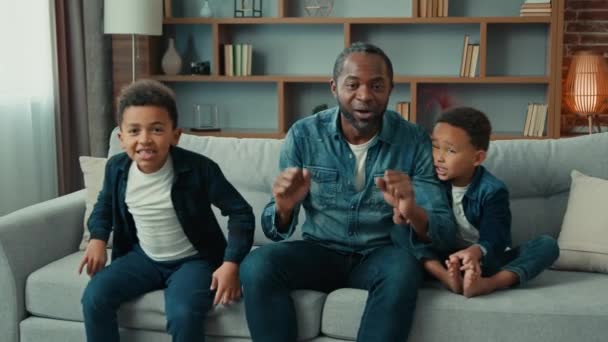 兴奋的非裔美国人快乐的家庭父亲和两个兄弟姐妹孩子们的孩子们 孩子们的粉丝们看电视体育比赛冠军庆祝目标电视队在体育比赛中的胜利坐在沙发上欢呼 — 图库视频影像