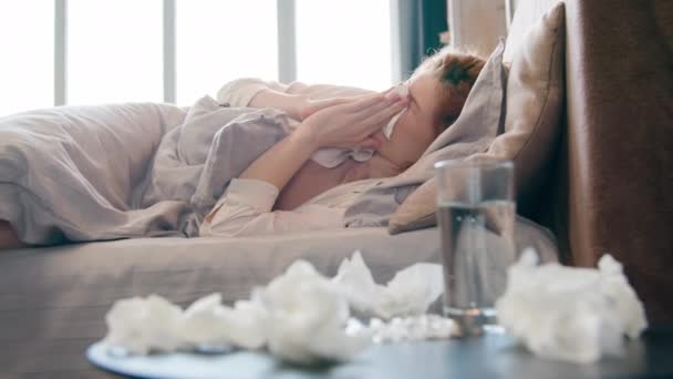 病気白人女性不健康な女の子に苦しみます熱風邪コロナウイルス季節性ウイルスアレルギー組織の鼻水を吹いてナプキンは 使用されたナプキンに囲まれたベッドのくしゃみに横たわって頭痛を感じます — ストック動画