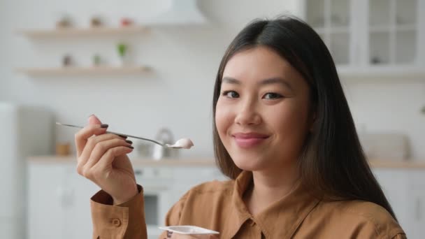 アジア系韓国人女性の味健康的な栄養は キッチンでクリーミーなフルーツヨーグルトを食べる中国人女の子笑顔カメラで食べる乳製品乳糖デザートとともにスプーン朝食フードロスウェイトダイエットヘルスケア — ストック動画