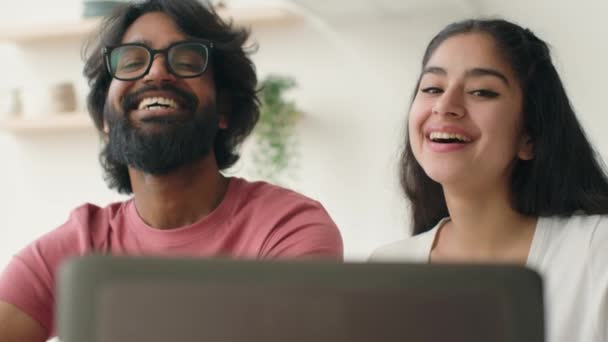 快乐的印度夫妇在厨房里用笔记本电脑笑着多样化的男人和女人上网看有趣的家庭照片在家里购物笑着和朋友们在网上聊天 — 图库视频影像
