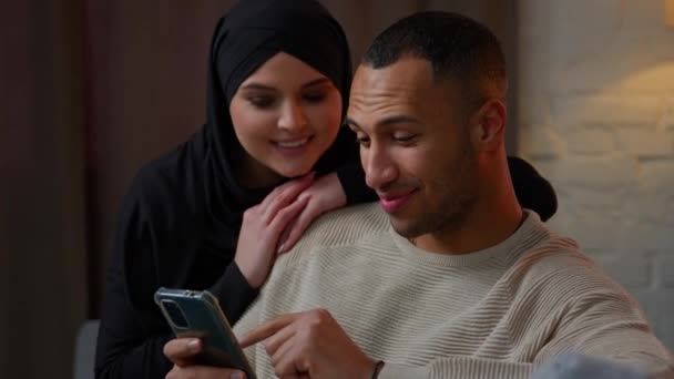 Wielorasowe Małżeństwa Używają Telefonu Komórkowego Domu Uśmiechnięta Muzułmanka Kobieta Żona — Wideo stockowe